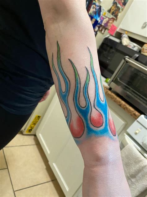 A Person With A Tattoo On Their Arm That Has Blue And Red Flames Coming