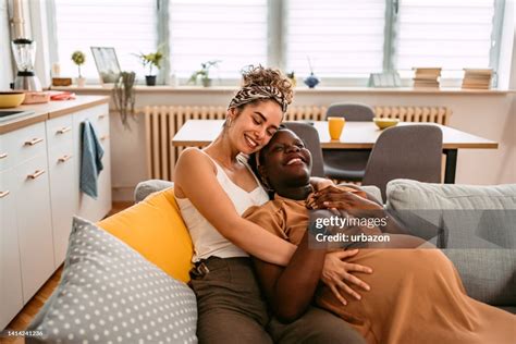 Pregnant Lesbian Couple Embracing Each Other On The Sofa High Res Stock