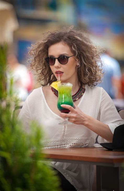 Happy Brunette Girl With Sunglasses And Black Hat Sitting At The Park