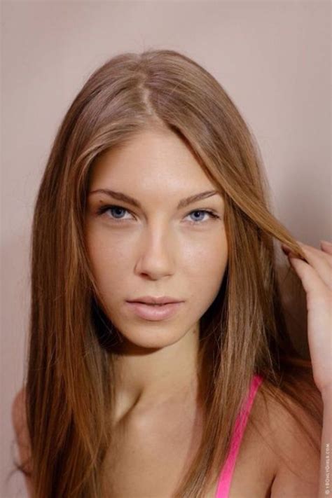 A Woman With Long Brown Hair And Blue Eyes Is Posing In Front Of A Pink