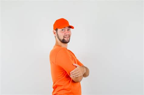 Free Photo Delivery Man In Orange T Shirt Cap Standing With Crossed