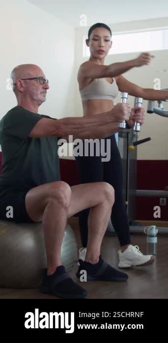 Vertical Shot Of Mature Man Exercising With Dumbbells Sitting On