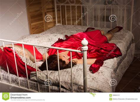 Brune Sensuelle Dans Une Robe Rouge Se Trouvant Sur Le Lit Photo Stock