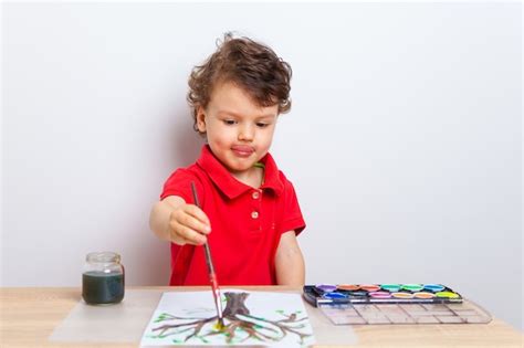 Premium Photo Cute Boy Drawing A Tree With Paints On A Paper Sheet