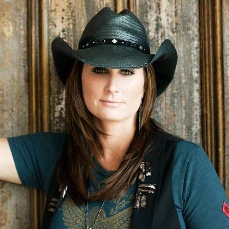 A Woman Wearing A Cowboy Hat Poses For A Photo In Front Of A Wooden Wall