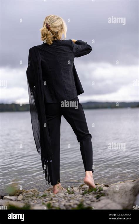 A Back View Of A Cool Barefoot Woman In A Black Suit Standing Near A