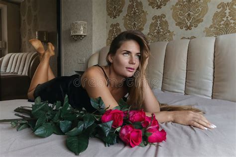 Una Mujer Se Sienta En La Cama Con Un Ramo De Rosas Rojas En El Regazo