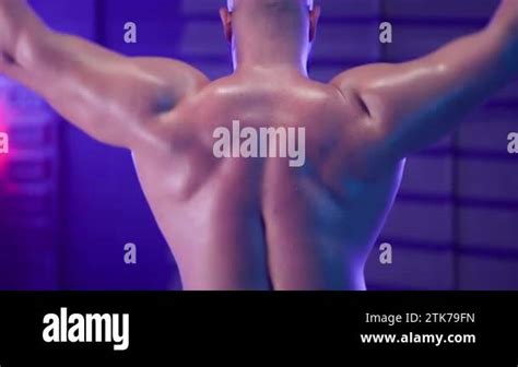 Back View Of Male Bodybuilder With Naked Torso Lifting Barbell From Behind His Head In Dark Gym