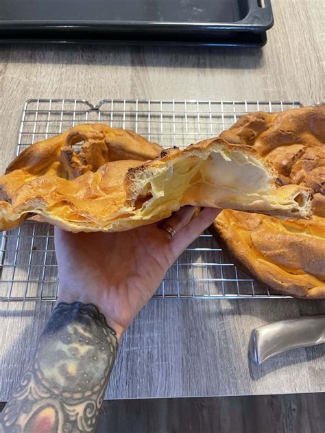 A Person Holding Up A Pastry On Top Of A Cooling Rack Next To A Knife