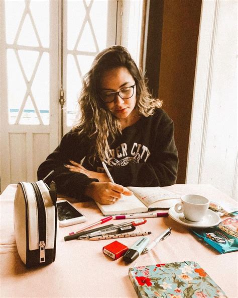 A Woman Sitting At A Table With Books And Pens In Front Of Her Writing