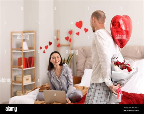 Young Man Surprising His Wife With Flowers And Balloon In Bedroom On