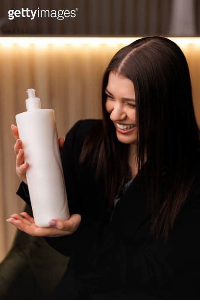 A Woman Smiles As She Holds A Bottle Of Shampoo In Her Hands