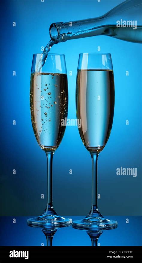 The Aromatic Champagne From The Bottle Is Poured Into Two Glasses On A Blue Background Stock