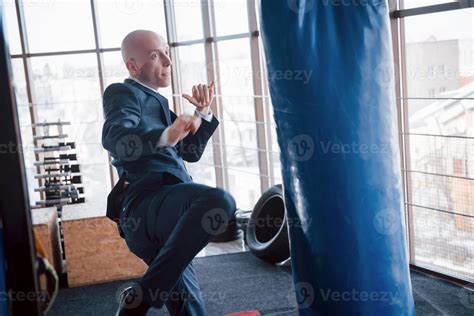 An angry bald businessman beats a boxing pear in the gym. concept of