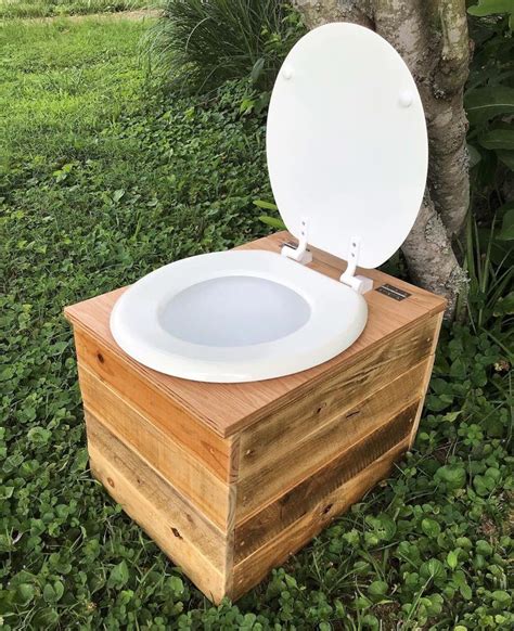 A Toilet Sitting On Top Of A Wooden Box In The Grass Next To A Tree