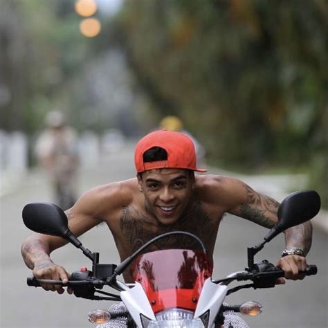 A Man Riding On The Back Of A Motorcycle Down A Street Next To Another