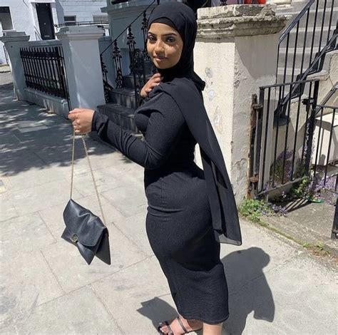 A Woman In A Black Dress And Hijab Poses For The Camera With Her Purse