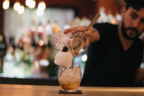 A Man Pours A Drink Into A Glass At A Bar With Ice Cubes