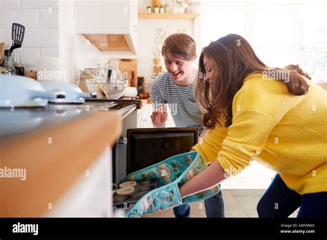 Young Downs Syndrome Couple Putting Homemade Cupcakes Into Oven In