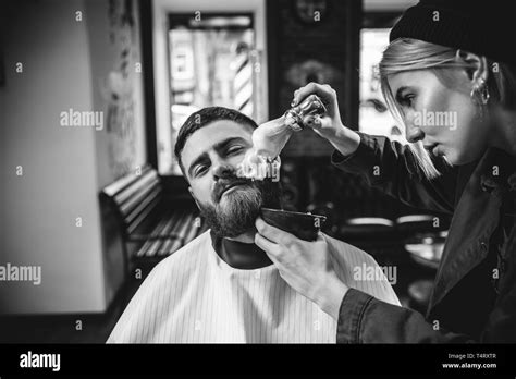 Client during beard shaving in barbershop. Female barber at salon ...