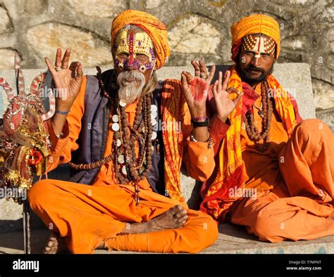 Two Sadhus Holy Men With Painted Faces Clad In Orange Robes Sit On