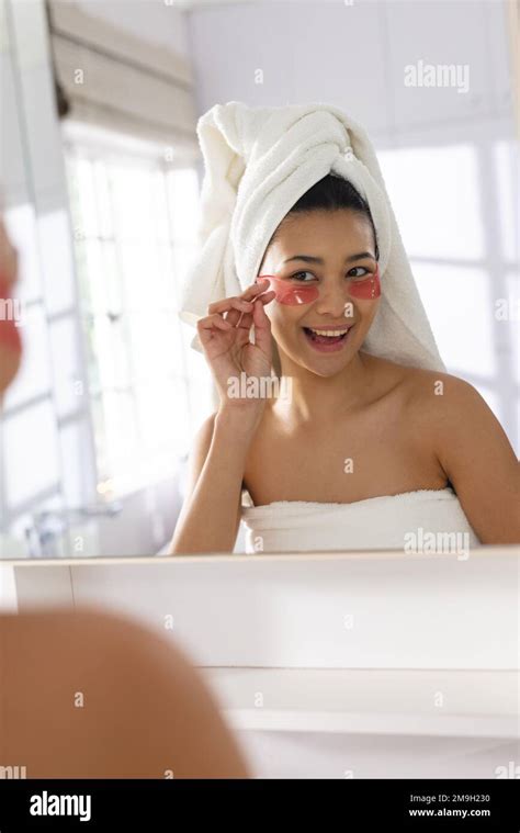 Image Of Biracial Woman With Towel On Head Applying Eye Mask In