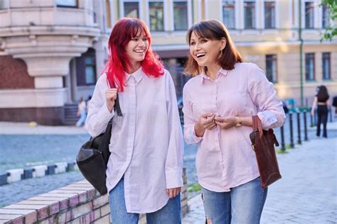 Mother And Teenage Daughter Walking Talking Together Along City Street