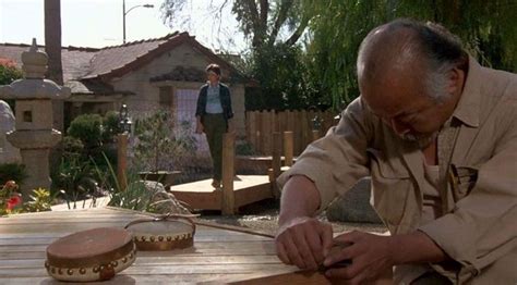 An Older Man Is Working On Some Kind Of Wooden Object In His Yard With Two Other Men Standing