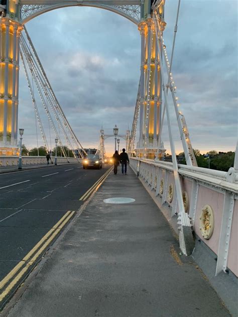 Two People Walking Across A Bridge At Dusk