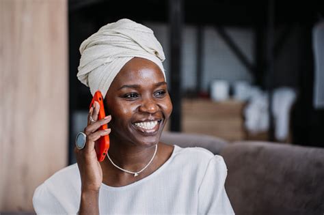 Woman In Elegant White Dress And Headwrap Smiles While Using Smartphone