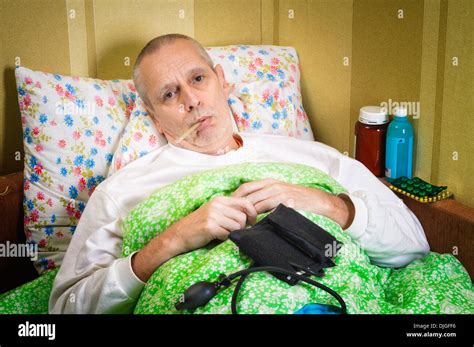 Sick Man Lying In Bed And Measuring The Temperature With A Thermometer