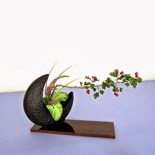 A Black Vase With Plants In It Sitting On A Wooden Stand Next To A