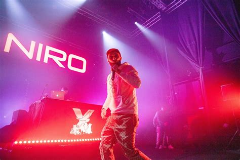 A Man Standing On Top Of A Stage In Front Of Purple And Red Lights With