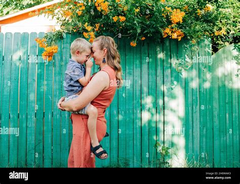 Mother Snuggles Little Boy While Standing In Front Of Green Fence Stock