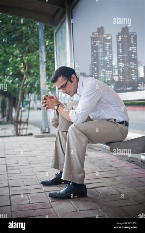 Businessman Sitting On A Bench At Bus Stop And Looking Thoughtful Stock