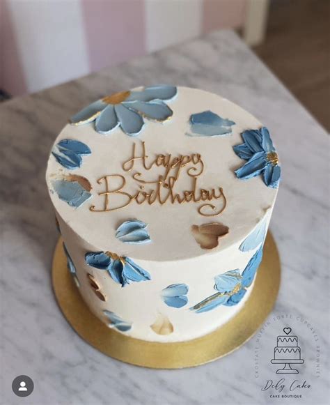 A White And Blue Birthday Cake With Flowers On The Top Is Sitting On A