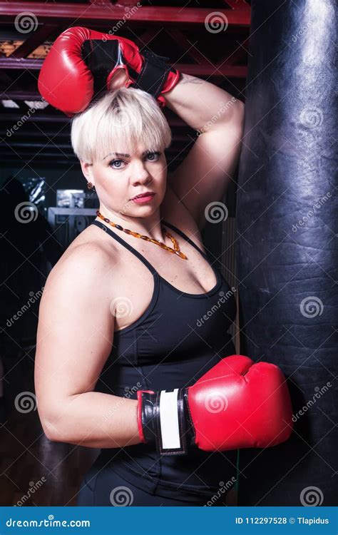 Mujer Hermosa Con Los Guantes De Boxeo Rojos Al Lado Del Saco De Arena