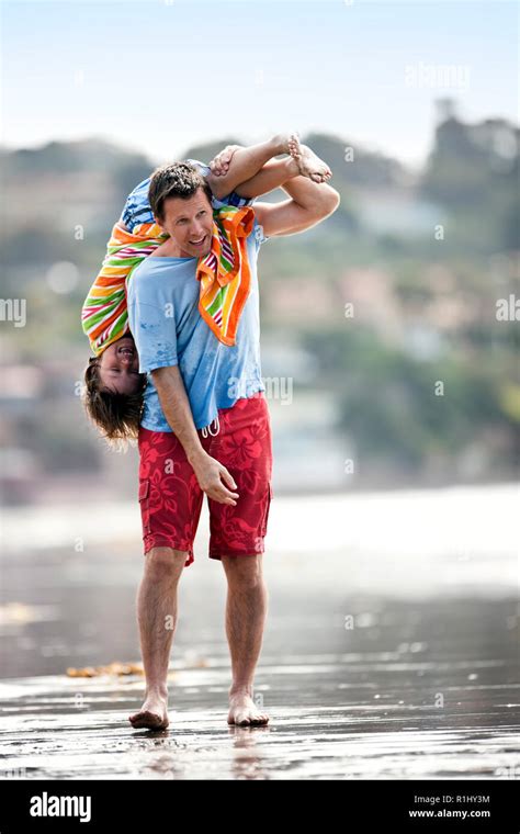 Father Carrying His Son Upside Down Over His Shoulder At The Beach