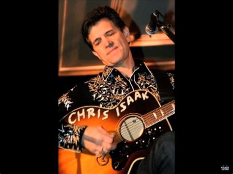 a man holding an acoustic guitar in his right hand and wearing a black shirt with gold lettering