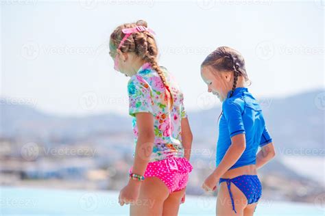 Adorable Little Girls On The Edge Of Outdoor Swimming Pool With