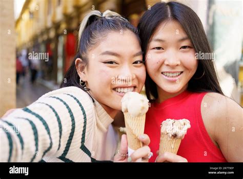 Two young Chinese girls taking a selfie while eating an ice cream cone ...