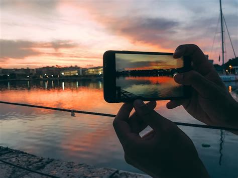 Manos de hombre tomando una foto con teléfono móvil de una puesta de