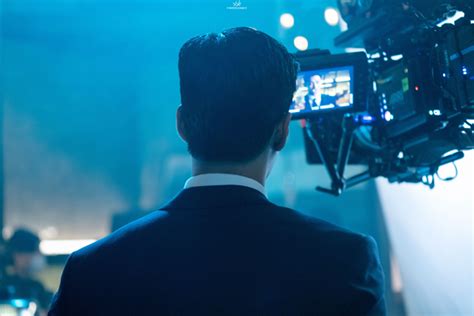 A Man Standing In Front Of A Camera On Top Of A Blue Stage With Lights