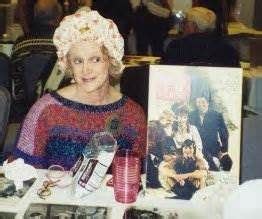 A Woman Is Sitting At A Table With Many Items On It And People In The