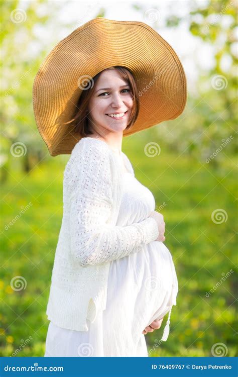 Pregnant Woman Wearing Big Hat And White Dress In Blooming Garde Stock