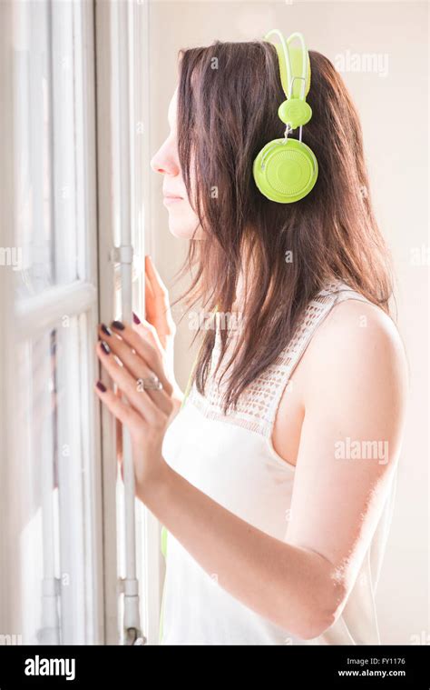 Woman Standing By A Window Looking Away She Is Listening To Music In