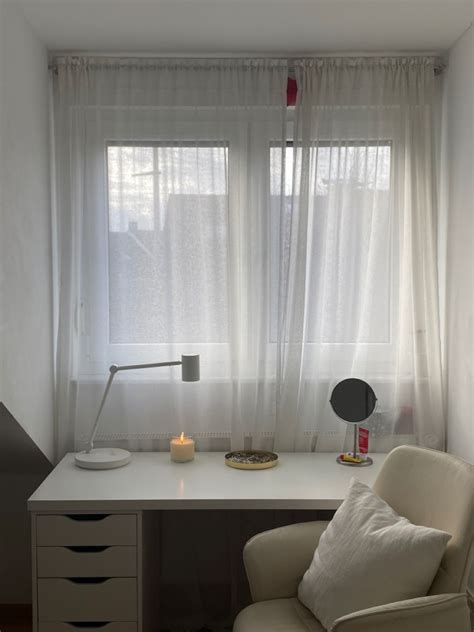 A White Chair Sitting In Front Of A Window Next To A Desk With A Lamp On It