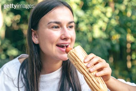 A Young Woman Eats A Hot Dog On A Cafe Terrace 이미지 1738744244 게티이미지뱅크