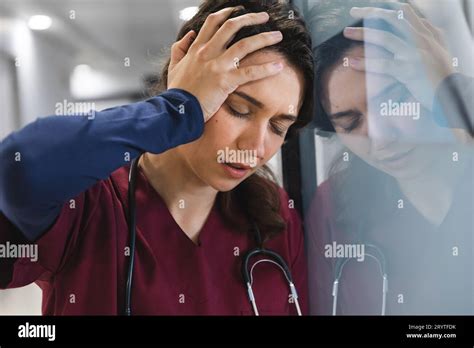 Tired caucasian female doctor wearing scrubs, leaning on wall in corridor at hospital Stock ...