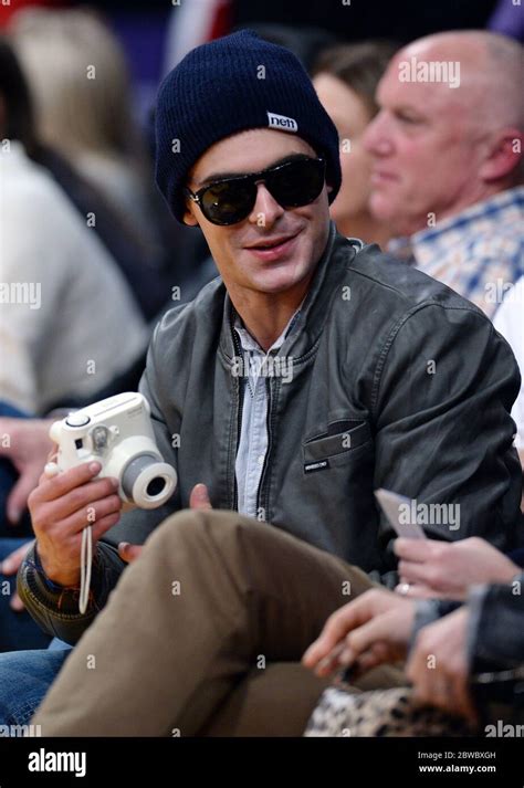 Zac Efron wearing beanie, holding camera at LA Lakers NBA game ...